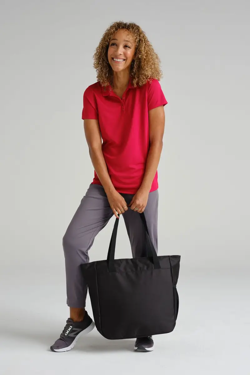 qulity product page 1 A woman stands with a black tote bag, wearing a red polo shirt and gray pants, with a casual athletic style.